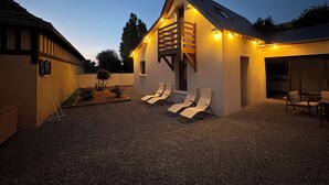 Ein modernes Haus mit Satteldach, einer kleinen Terrasse mit Liegestühlen und einem Schotterweg.
