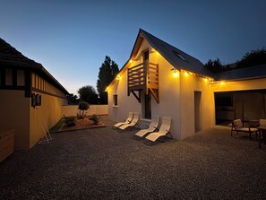 A modern house with a sloped roof, a small deck with lounge chairs, and a gravel driveway.