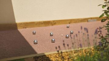 A wooden deck with metal balls and a white ball, surrounded by plants.