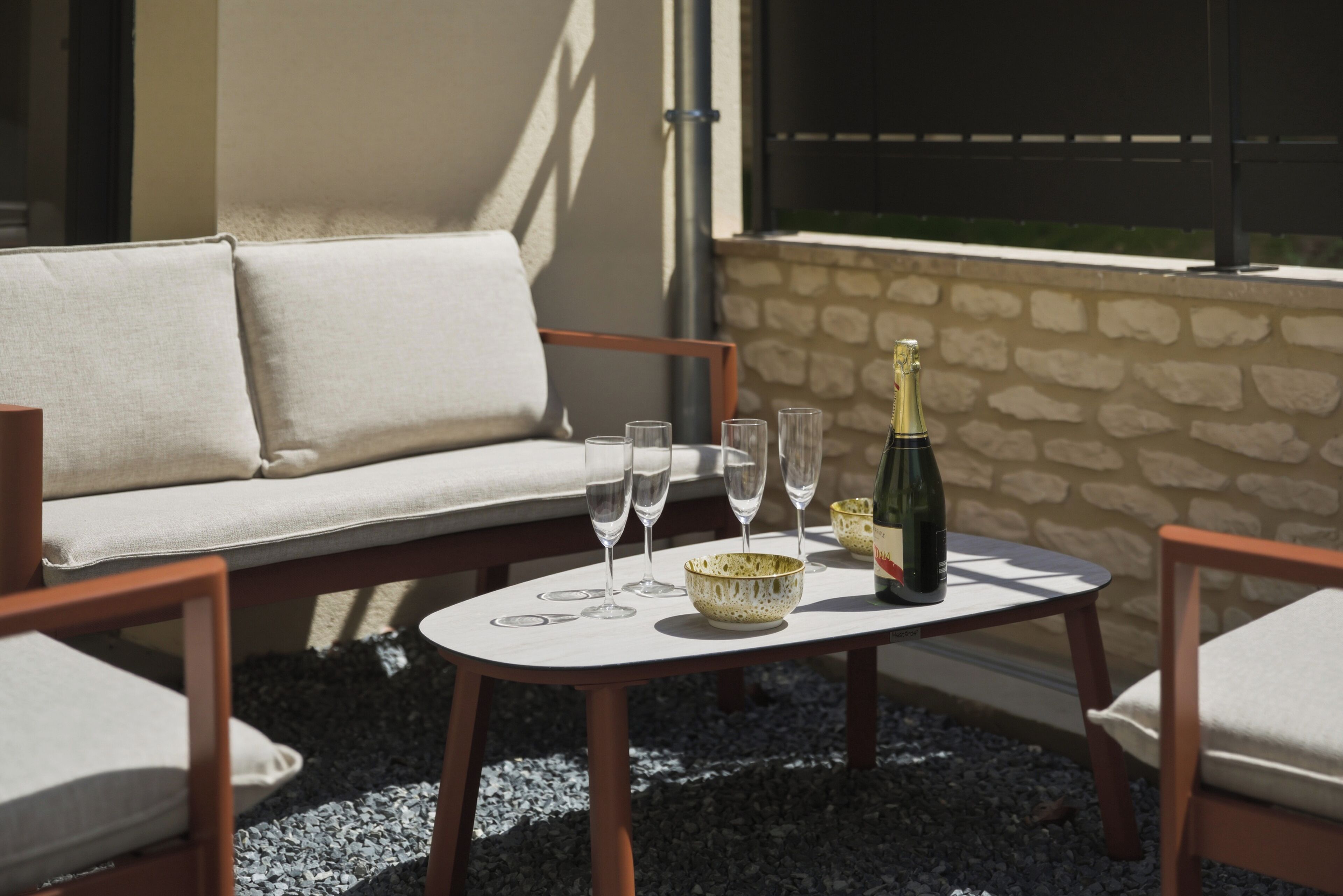Eine Terrasse mit einem weißen Tisch, einer Champagnerflasche und mehreren Gläsern.