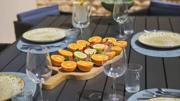 Uma mesa de jantar posta com pratos, talheres, copos e uma travessa de frutas.