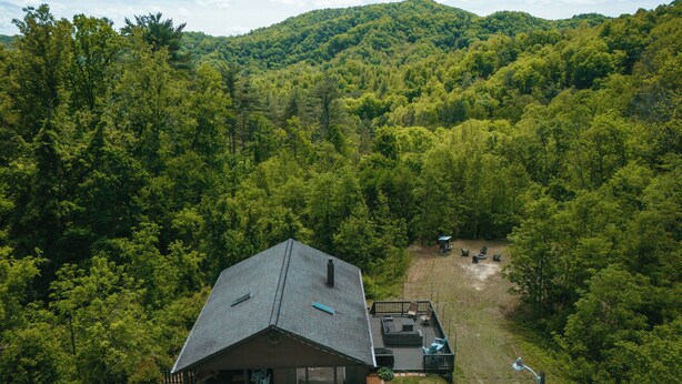 A cabin with a deck, surrounded by dense forest and hills.