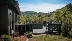 A deck with outdoor seating, a view of a forested hillside, and a building with a dark exterior.