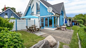 Una casa de dos plantas con fachada azul, una antena parabólica y un patio con mobiliario exterior.