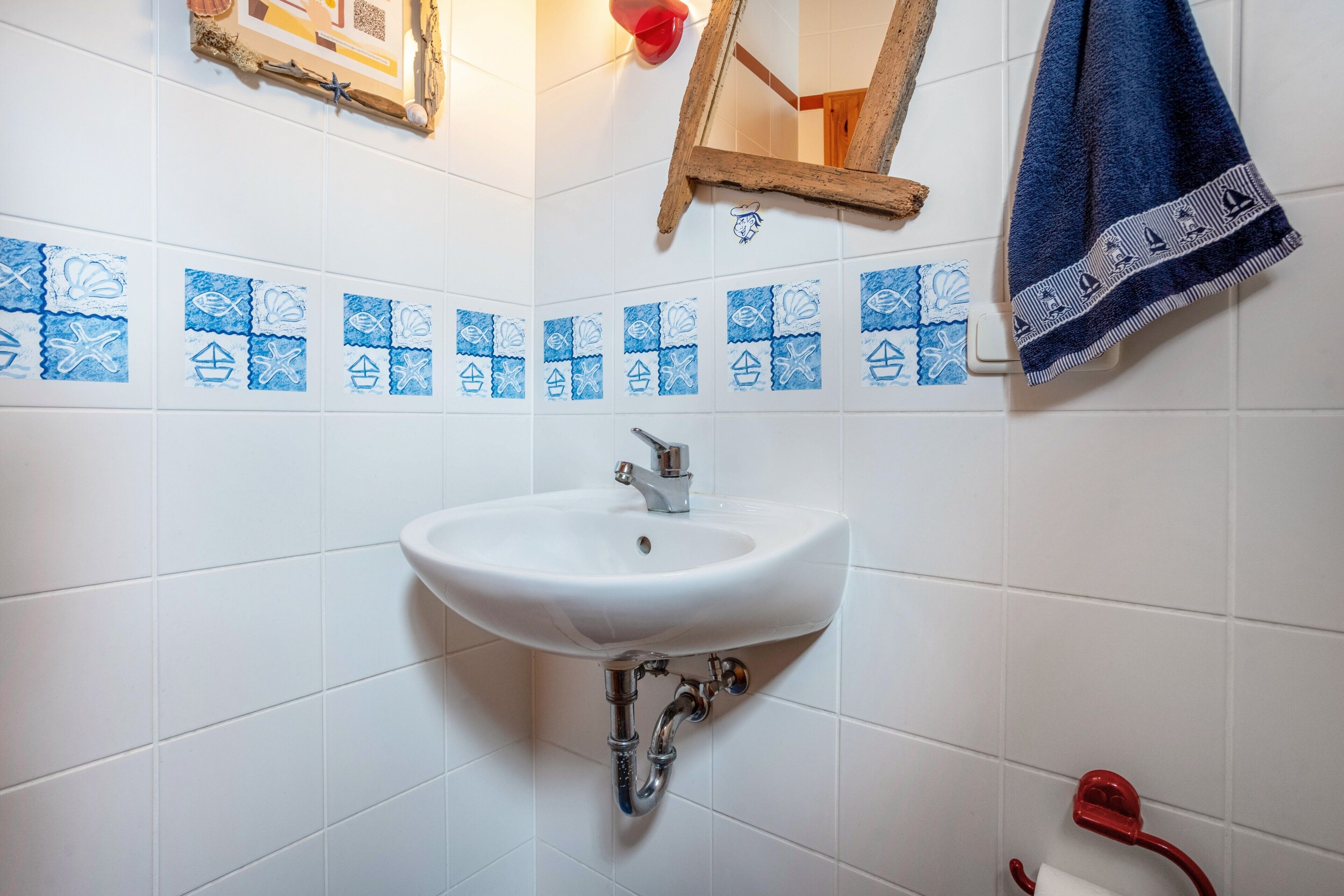 A bathroom with a white sink, blue decorative tiles, a wooden-framed mirror, and a red towel rack.