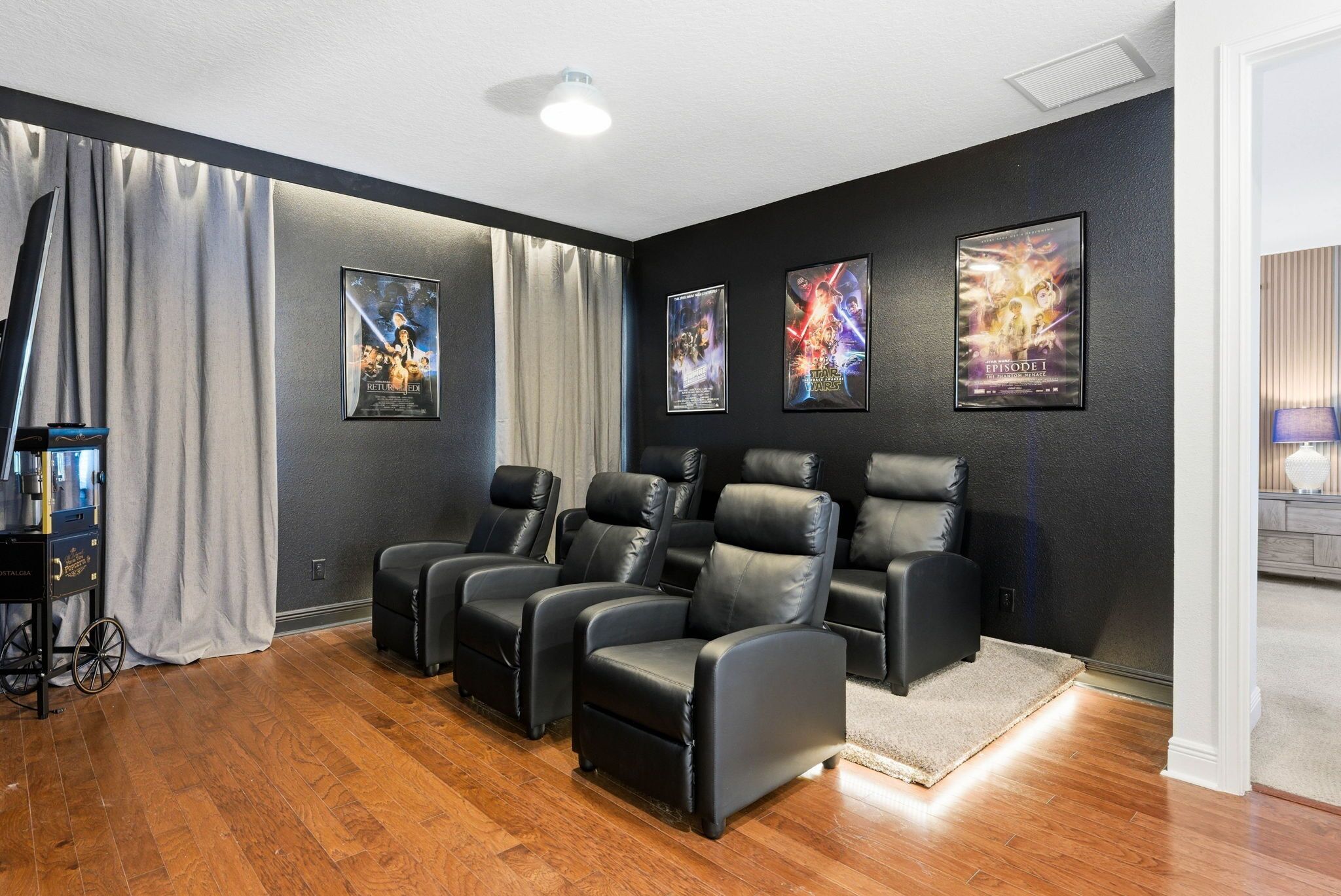 A home theater room with black leather recliners, a popcorn machine, and movie posters on the wall.
