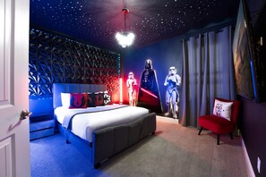 Ein Schlafzimmer mit einem Bett, einer Decke mit Sternenhimmel, Wandbildern zum Thema Star Wars und einem roten Sessel.