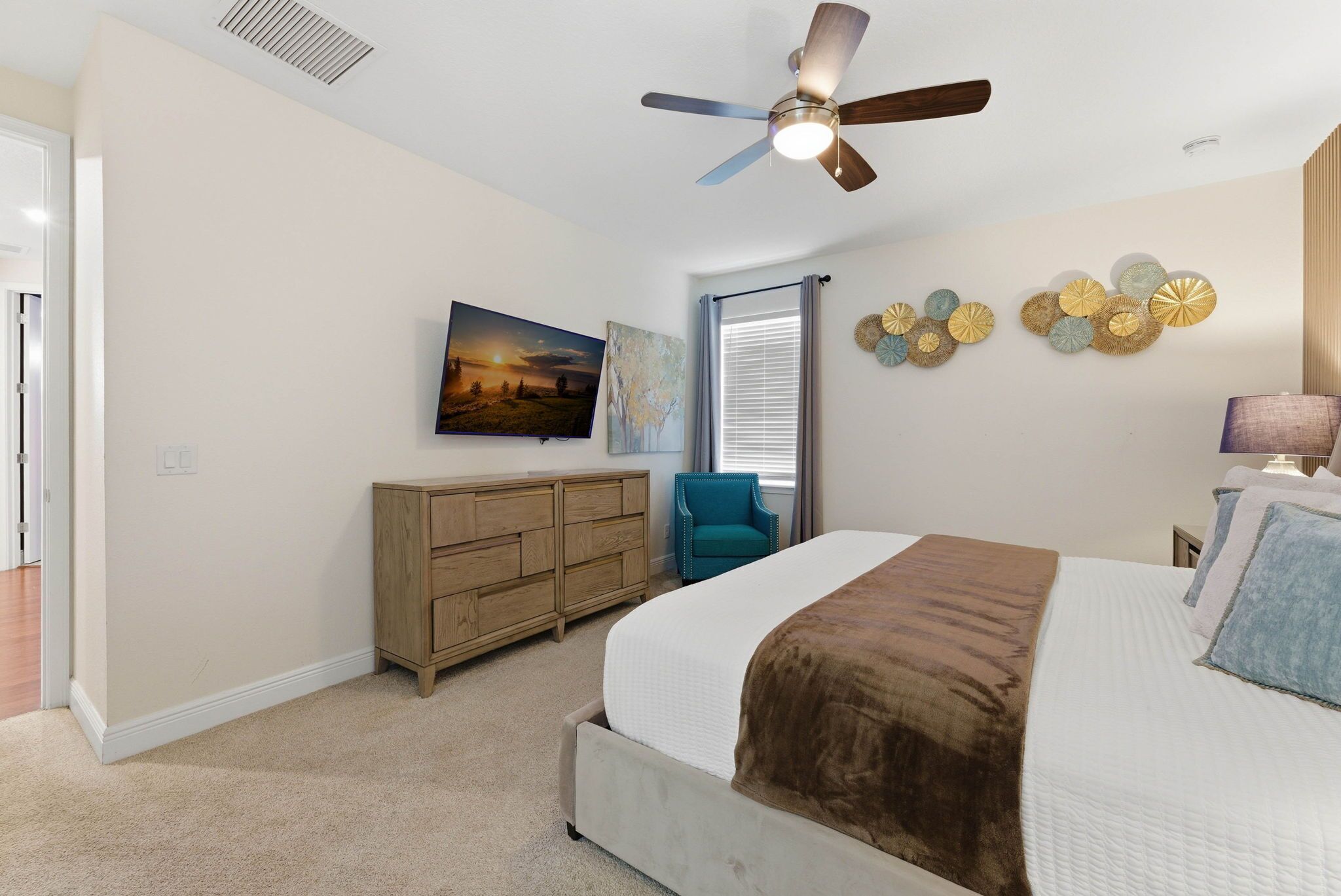 A bedroom with a bed, a ceiling fan, a dresser, a chair, and wall decorations.
