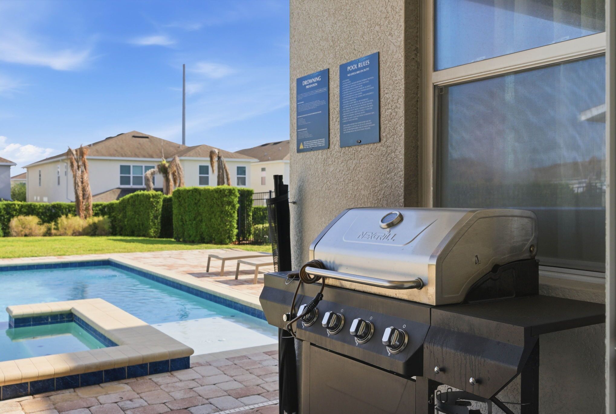 Un barbecue a bordo piscina con vista su una piscina e un'area residenziale sullo sfondo.