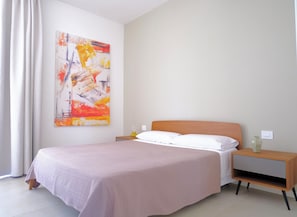 A bedroom with a bed, a nightstand, a lamp, and a painting on the wall.