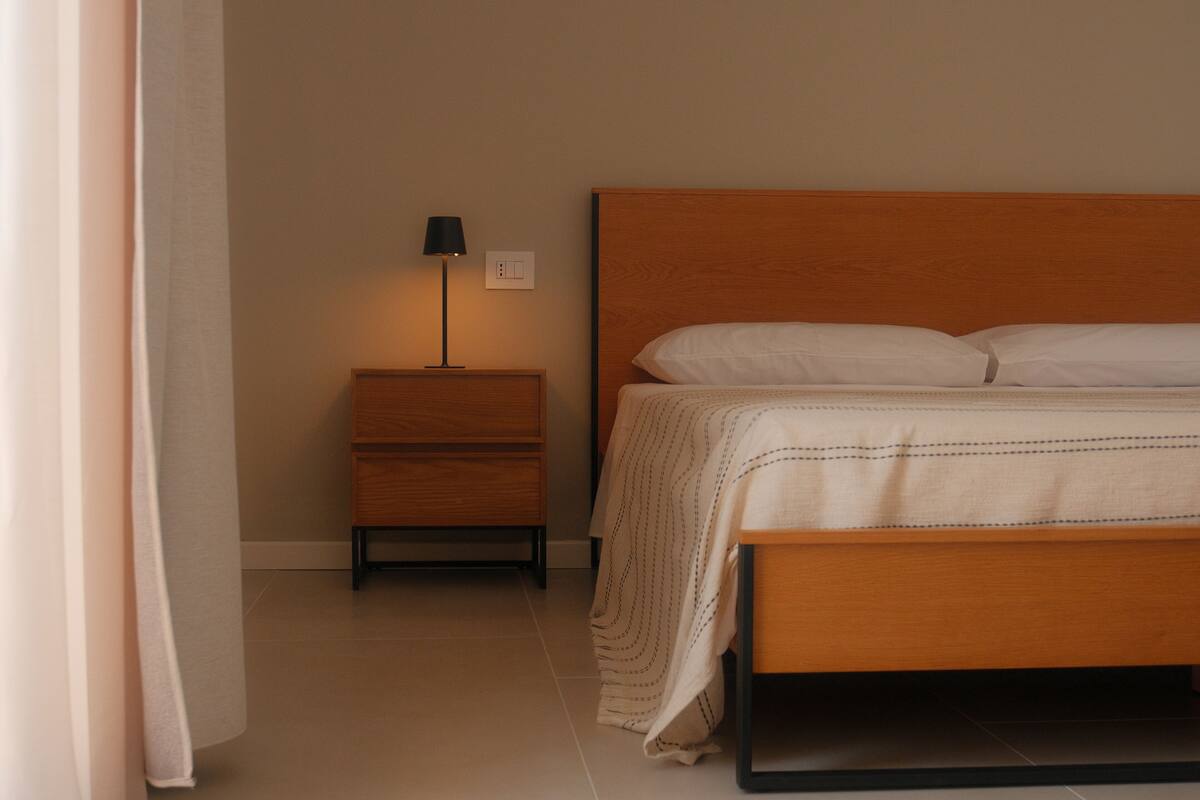 Un dormitorio con una cama de madera, una mesita de noche con lámpara y un mueble auxiliar.