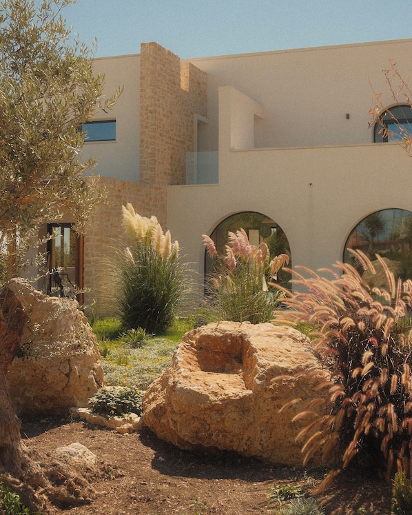 A modern building with a stone facade, arched windows, and a landscaped garden with rocks and plants.