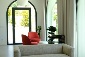 A modern living room with a sofa, a red chair, a small table with a plant, and a door leading outside.