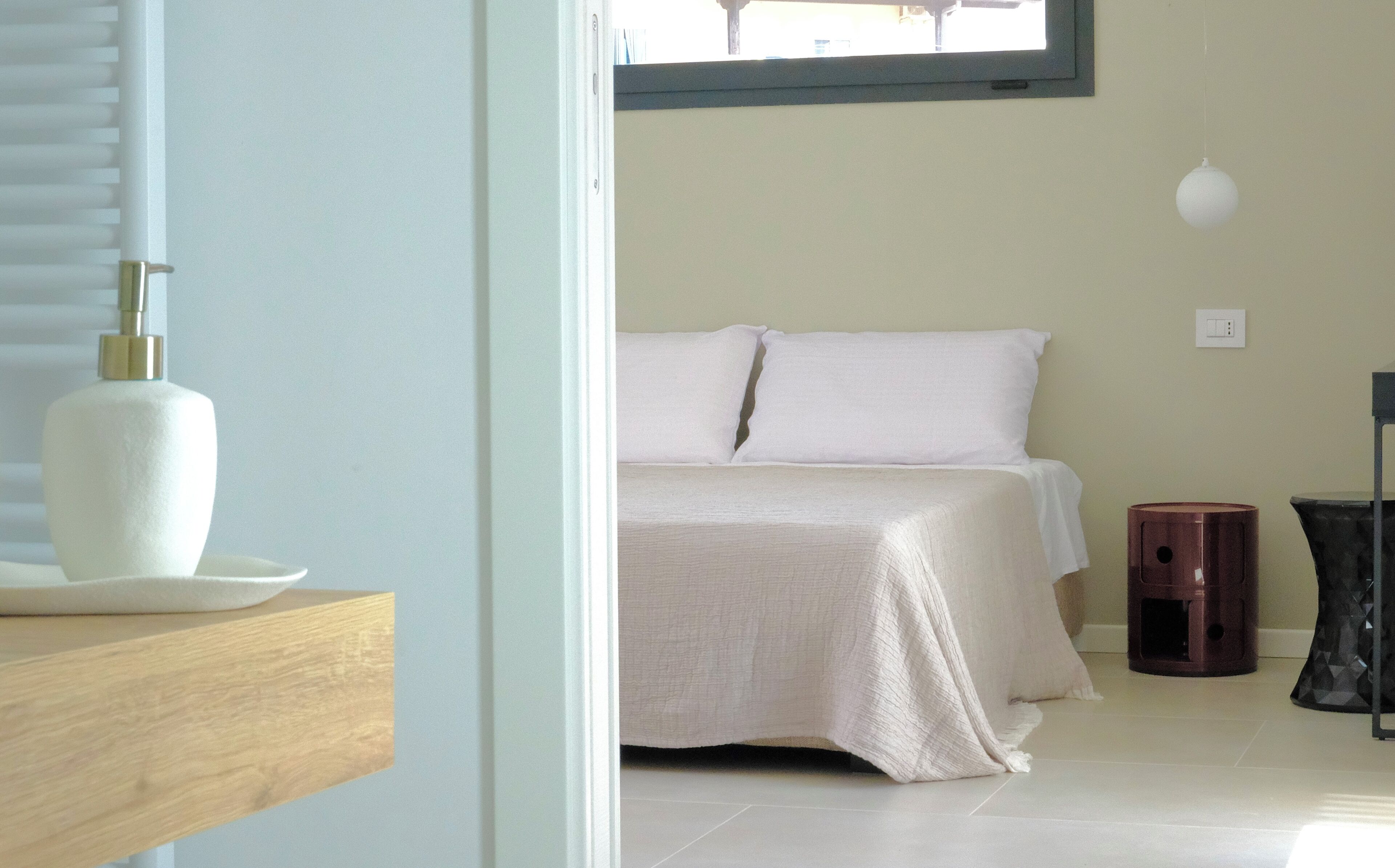 A bedroom with a bed, a bedside table, a lamp, and a trash bin.