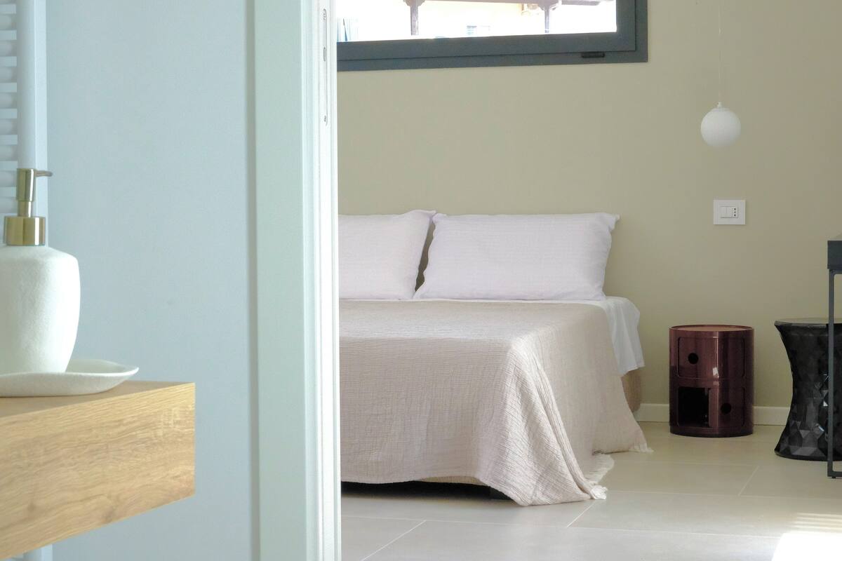 Un dormitorio con una cama, una mesita de noche, una lámpara y un cubo de basura.