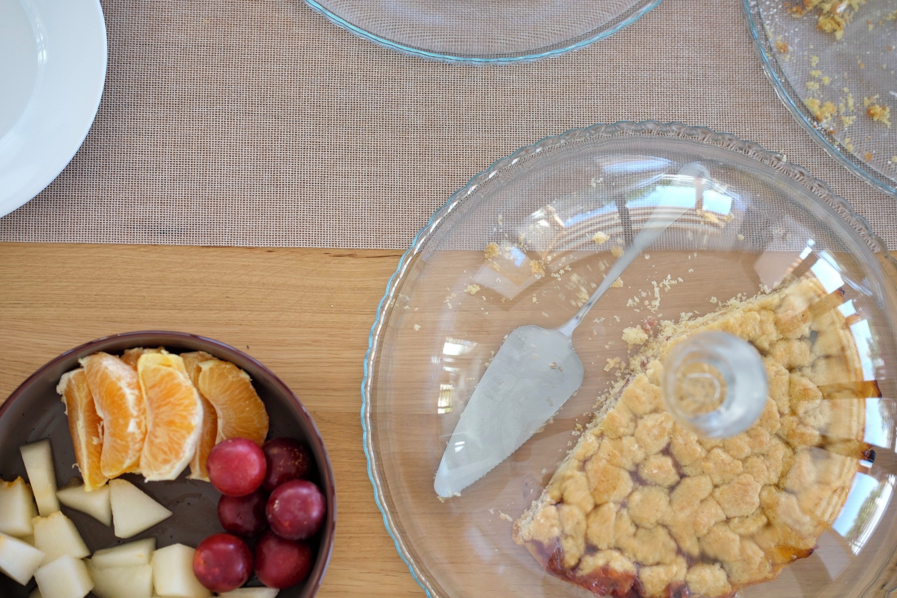A clear glass pie dish with a crumbly pie crust and a slice on a wooden table.