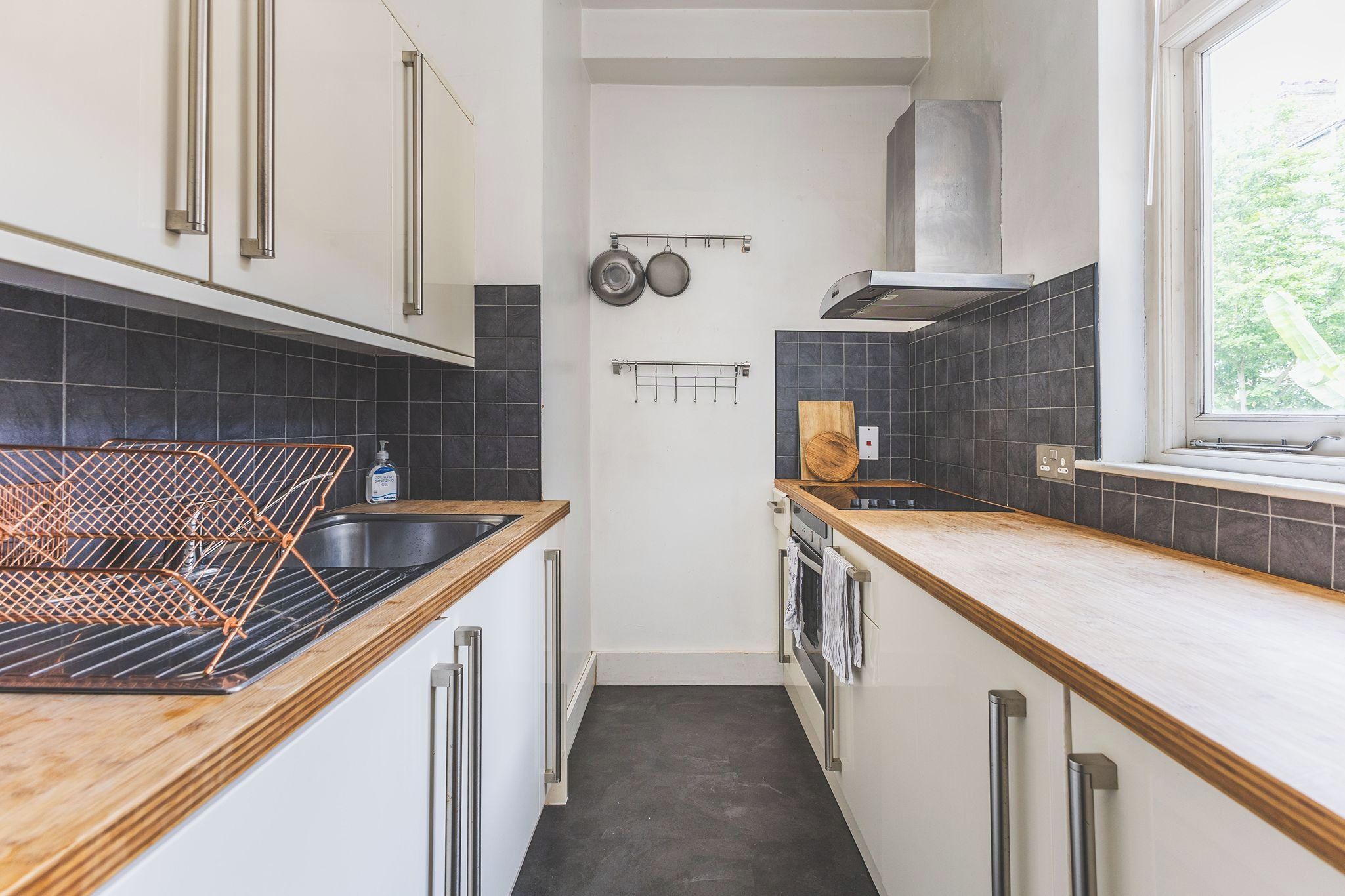 Eine moderne Küche mit einem Edelstahlspülbecken, Holz Arbeitsplatten und einer schwarzen gefliesten Spritzschutzwand.