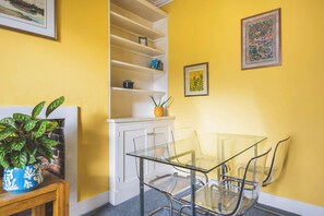 Ein Zimmer mit Glastisch und -stühlen, einem weißen Schrank und einer Topfpflanze.