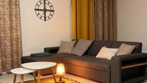 Ein modernes Wohnzimmer mit einer Couch, zwei kleinen Tischen, einer Lampe und einer Wanduhr.