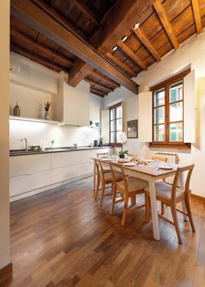 A spacious kitchen with wooden beams, white cabinets, and a dining area with wooden chairs. - Pilastri 44 Cozy Apt in the Heart of Florence (Firenze)