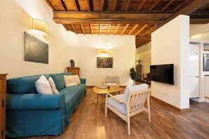Un salon comprenant un canapé, un fauteuil, une table, un téléviseur et un coin cuisine.
