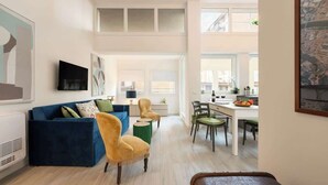 Ein modernes Wohnzimmer mit einem blauen Sofa, einem gelben Sessel und einem Essbereich mit Tisch und Stühlen.