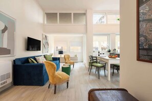 Un salon moderne avec un canapé bleu, un fauteuil jaune et un coin repas comprenant une table et des chaises.