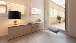 Ein modernes Interieur mit einem hellen Konsolentisch, einer Stehlampe und Blick durch eine Glastür auf einen Außenbereich mit Topfpflanzen.