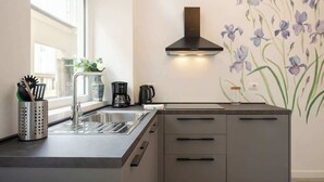 Eine moderne Küche mit Spüle aus Edelstahl, einer schwarzen Dunstabzugshaube und einer wandmontierten Kaffeemaschine.