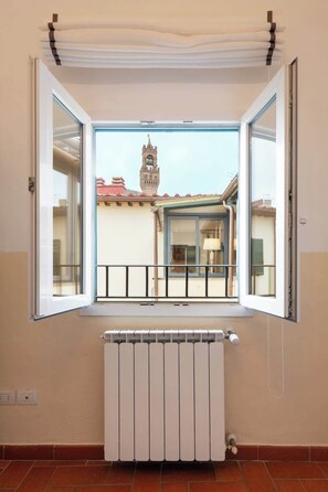 Ein Zimmer mit Heizkörper, einem Fenster mit Blick auf ein Gebäude mit einem Glockenturm und einem Balkongeländer.