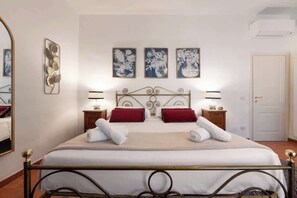 Ein Hotelzimmer mit einem Bett, zwei Nachttischen, einem Spiegel und drei an der Wand hängenden Kunstwerken.
