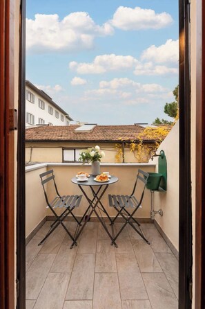 Ein Balkon mit Tisch, Stühlen, einer Topfpflanze und einem grünen Grill.