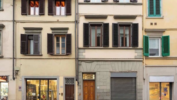 A row of multi-story buildings with shuttered storefronts, a visible door, and a small window with a view. - Guelfa Spacious New Elegant Central Position (Firenze)