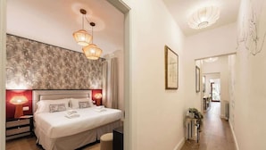 A hotel room with a large bed, two bedside lamps, a nightstand, a small stool, and a hallway leading to another room. - Guelfa Spacious New Elegant Central Position (Firenze)