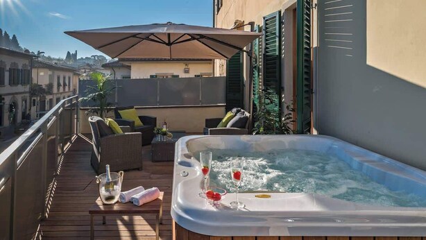 Een dakterras met een jacuzzi, buitenmeubilair en een grote parasol.