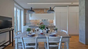 Een moderne eethoek met een bakstenen muur, hanglampen en een keuken op de achtergrond.
