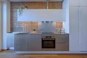 A modern kitchen with a brick wall, stainless steel appliances, and a white upper cabinet. - Solatio + Toscano assieme · Terrazza Jacuzzi in centro a Greve, 2 appartamenti (Greve in Chianti)