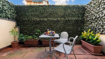 Un patio con tavolo e sedie, circondato da piante in vaso e un muro verdeggiante.