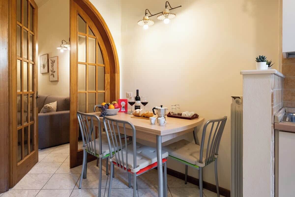 Zona pranzo con tavolo, sedie e angolo cottura con frigorifero.