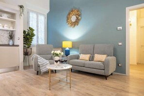 A living room with a grey sofa, a small round table with drinks, a lamp, and a decorative wall piece. - Reparata Wide Beautiful 10 min to Train Station (Firenze)