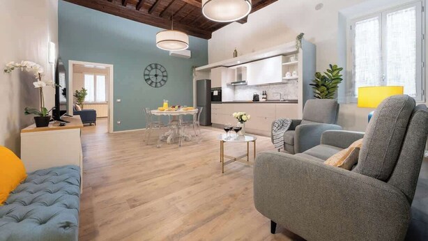 Ein modernes Wohnzimmer mit einer Couch, einem Sessel, einem Esstisch und einer Küche im Hintergrund.