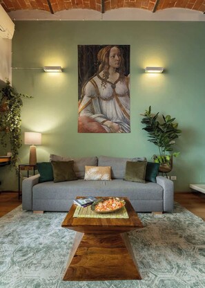A living room with a sofa, a coffee table with food, a painting on the wall, and two wall-mounted lamps. - Cimabue Design Loft in a Cool Area of Florence (Firenze)