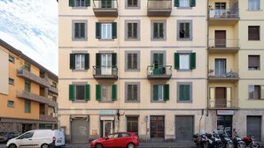 Un edificio de varios pisos con balcones, una camioneta blanca estacionada y un coche rojo en la calle.