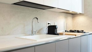 Cocina moderna con encimera blanca, pileta de acero inoxidable, cafetera y campana extractora.