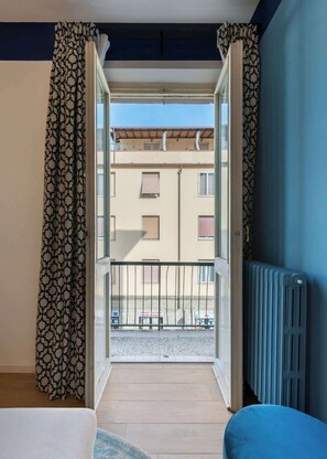 Een balkon met uitzicht op een gebouw, een radiator en gordijnen met een patroon.