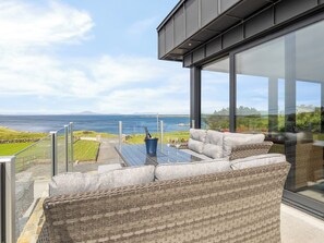 A balcony with a glass table, wicker furniture, and a view of the sea. - Brentwood/Luxury Ocean View Retreat in Connemara (Renvyle, Connemara)