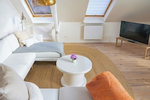 Ein modernes Wohnzimmer mit einer Couch, einem Couchtisch mit einer Blume, einem Fernseher auf einem Schrank und einem Dachfenster.