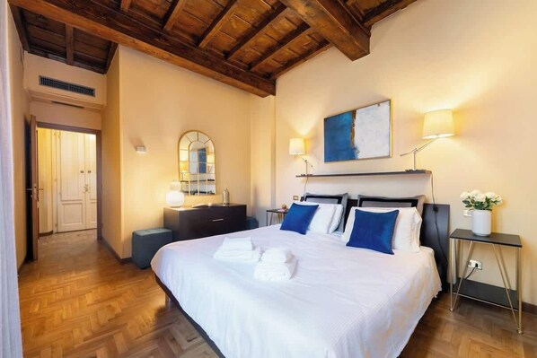 Ein Hotelzimmer mit einem großen Bett, Holzbalken an der Decke, einem Nachttisch mit Lampe, einem Spiegel und einem Bild an der Wand.