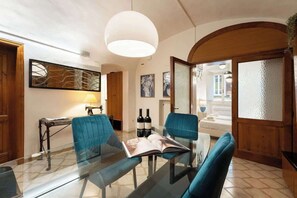 A modern living room with a glass table, blue chairs, a hanging light fixture, and a view of the street. - Egidio Spacious and bright 300mt from the Duomo (Firenze)