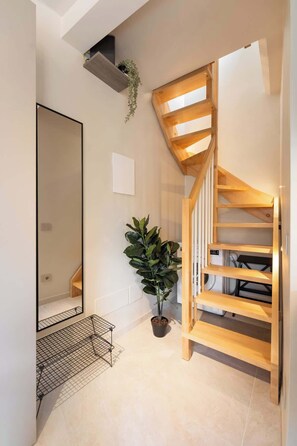 Ein modernes Interieur mit einer Holztreppe, einem großen Spiegel, einer Topfpflanze und einem Metallregal.